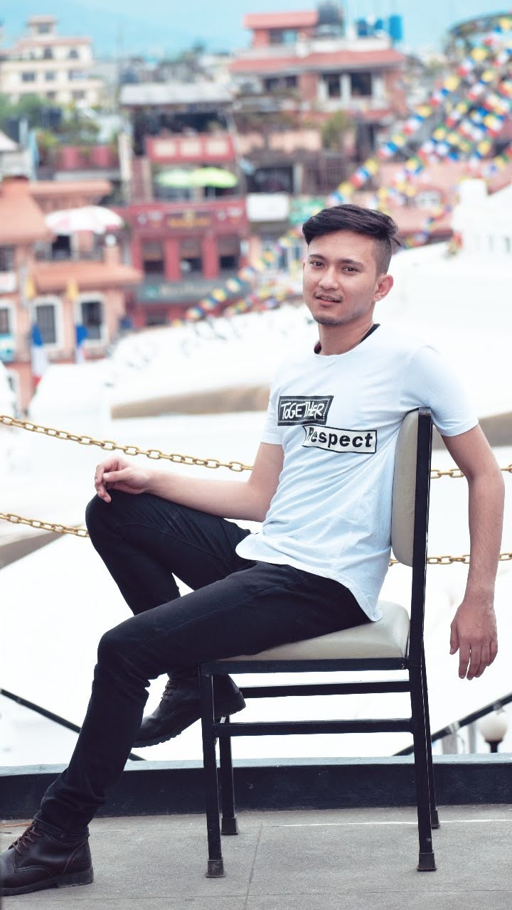 Nepali Boy Wilson Shrestha in a white T-shirt sitting infornt of bouddha sutpa. Sitting in a chair